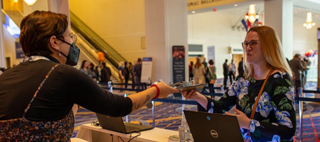 A person working at a registration desk handing materials to a happy registrant.